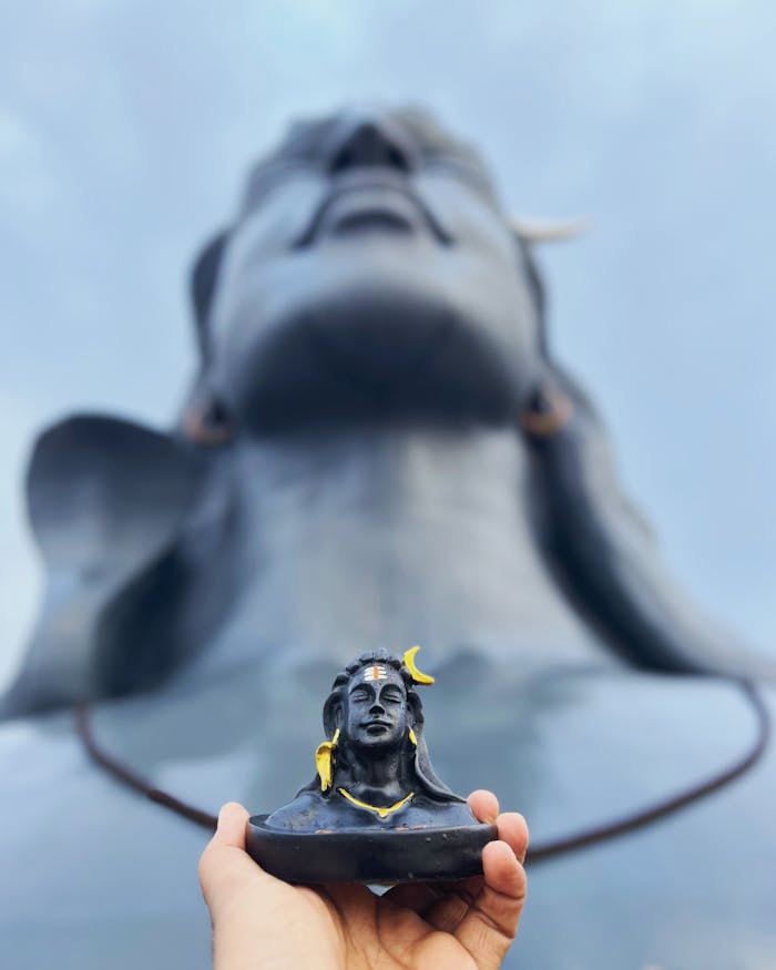 Close-up of a hand-held Adiyogi figurine against the monumental statue in Coimbatore.